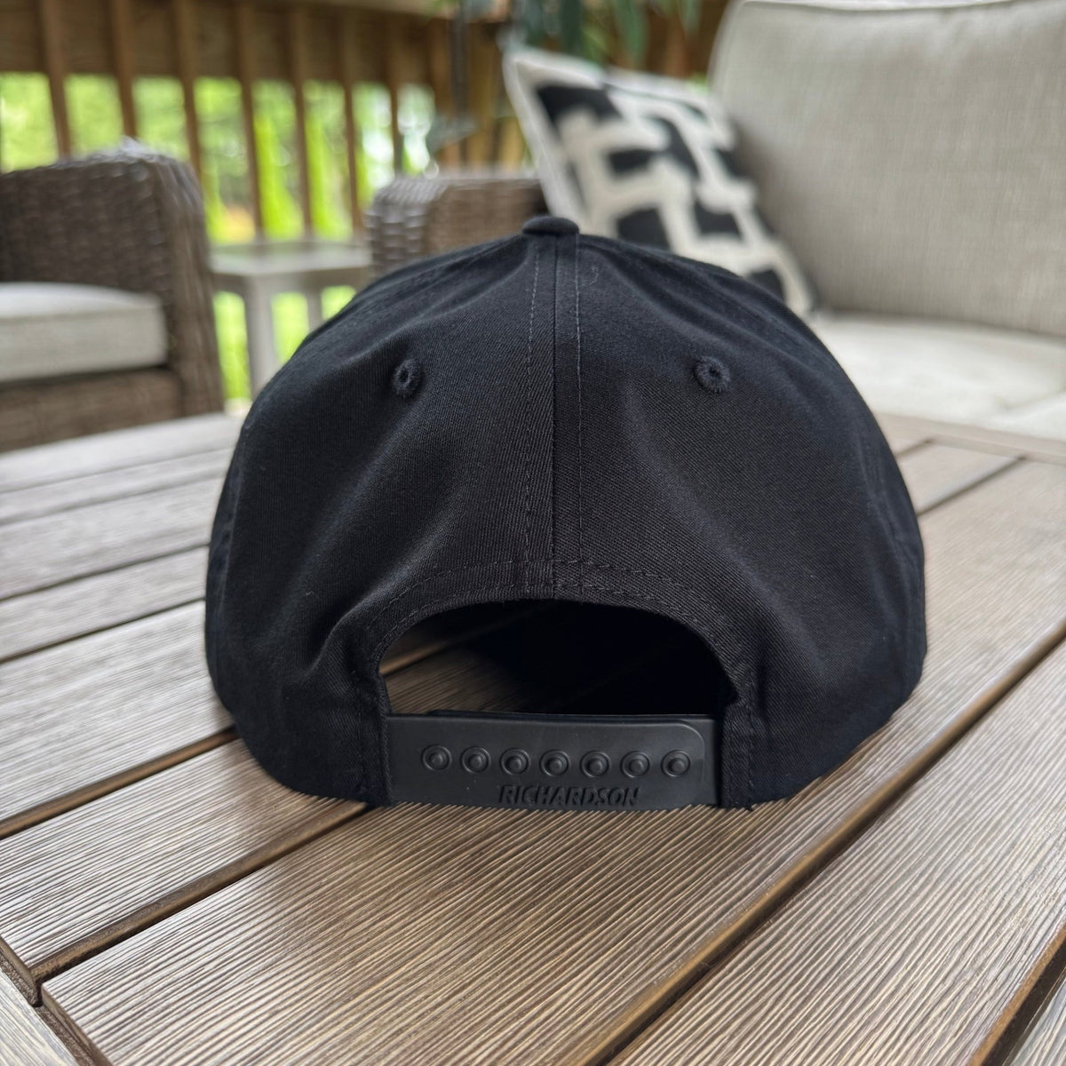 A FLOWAV Midnight Edition Richardson R255 showing the back snapback adstable hat feature in black. Set on a weathered wood outdoor table