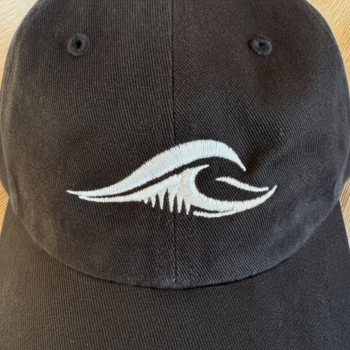 Close-up of the FLOWAV wave logo embroidered in cream thread on a black Richardson R55 baseball hat