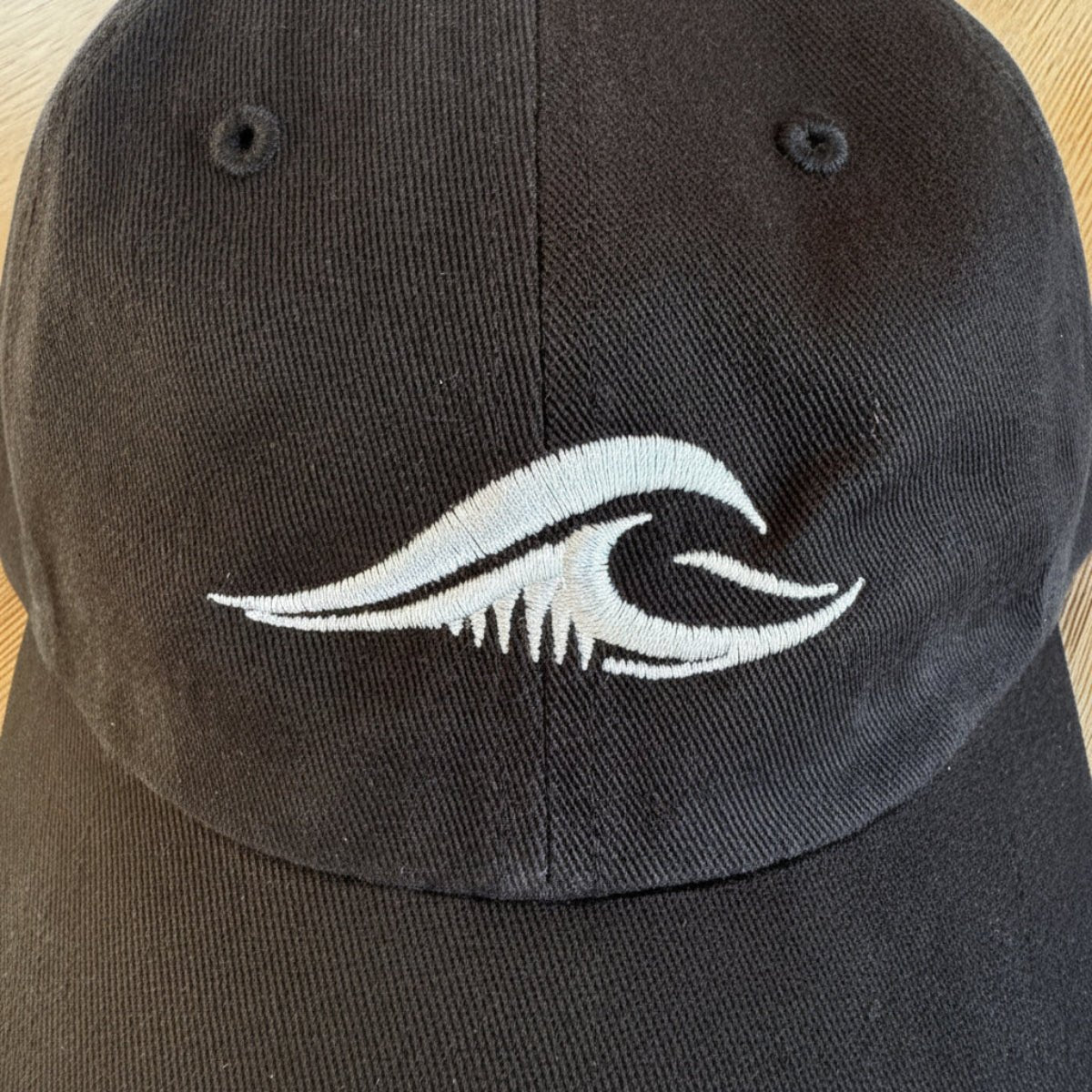 Close-up of the FLOWAV wave logo embroidered in cream thread on a black Richardson R55 baseball hat