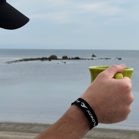 FLOWAV Breakaway Wristband worn by the ocean while holding a green mug.