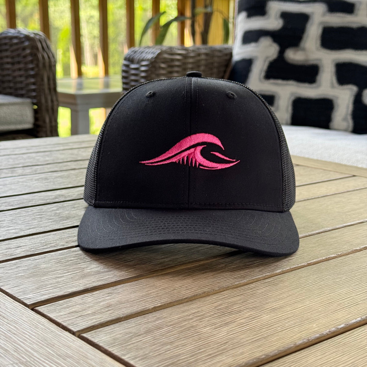 FLOWAV Pink Edition Richardson R112 Trucker Hat showing the front pink embroidered wave resting on a wooden table.
