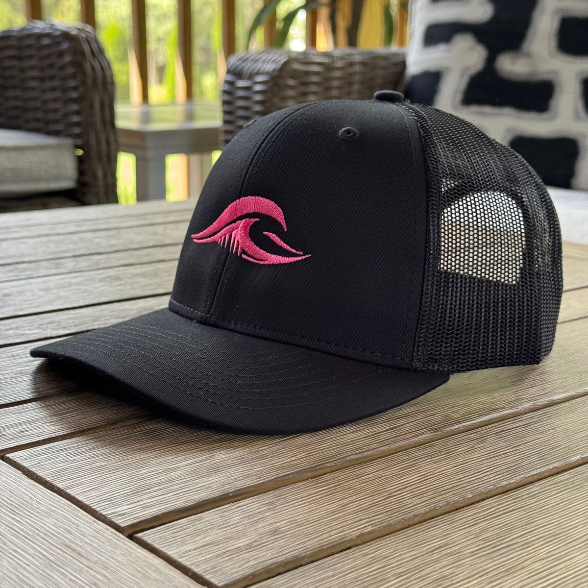 FLOWAV Pink Edition Richardson R112 Trucker Hat in black showing an angled view resting on a wooden table.