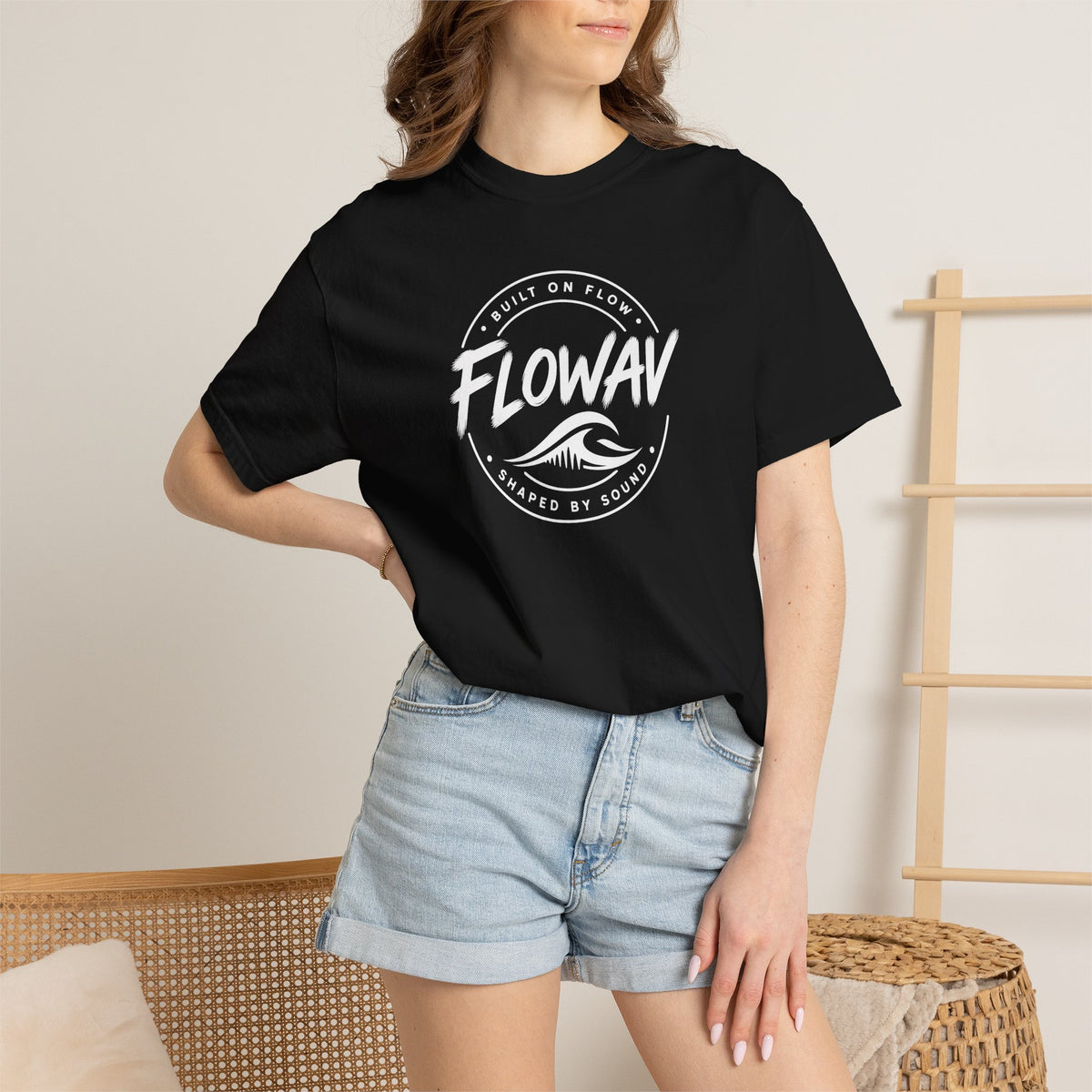 A woman wearing the FLOWAV Coastal Badge Tee in black showing the front coastal graphic and built on flow shaped by sound.
