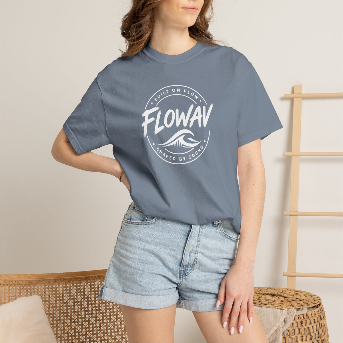 A woman wearing the FLOWAV Coastal Badge Tee in blue jean showing the front coastal graphic and built on flow shaped by sound.