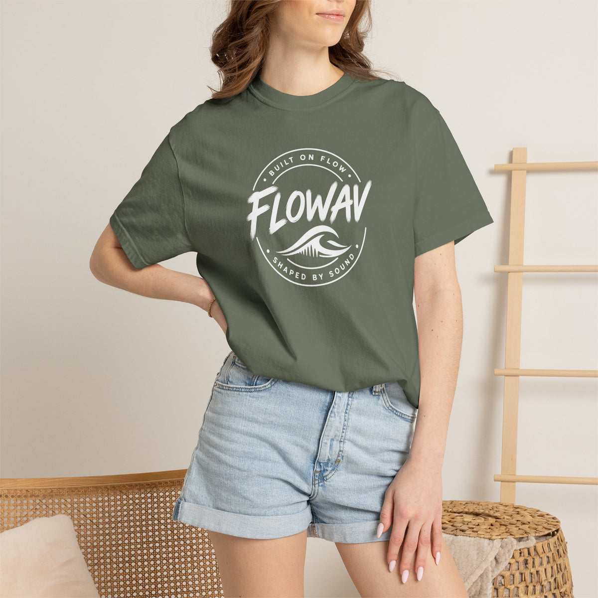 A woman wearing the FLOWAV Coastal Badge Tee in moss showing the front coastal graphic and built on flow shaped by sound.