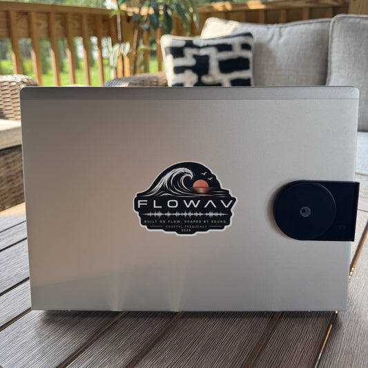 A FLOWAV Coastal Frequency Sticker on the back of a silver laptop on a wood table outside on a deck.