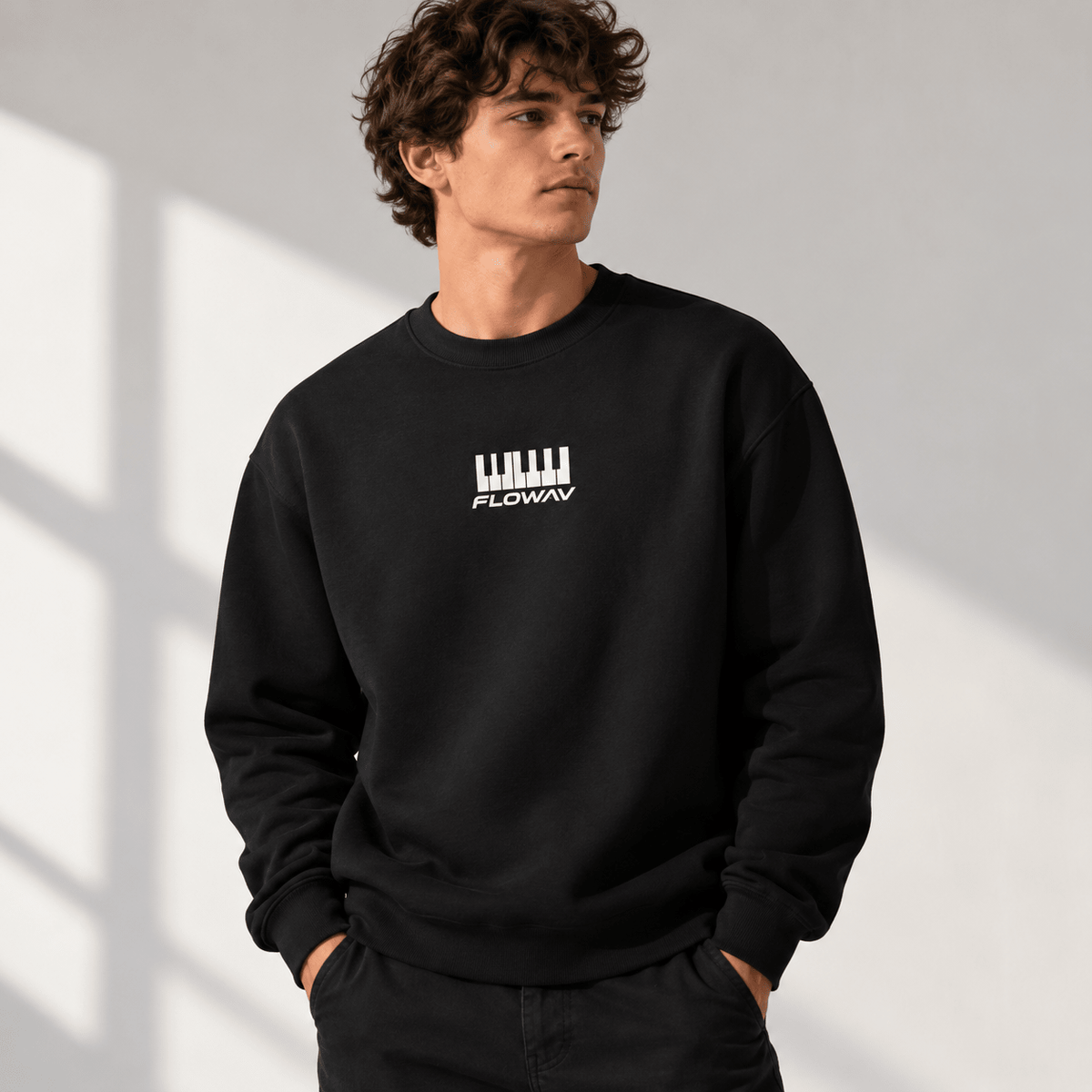 Man with long wavy hair wearing the FLOWAV Keys Crewneck Sweatshirt in black showing the piano keys and wordmark.