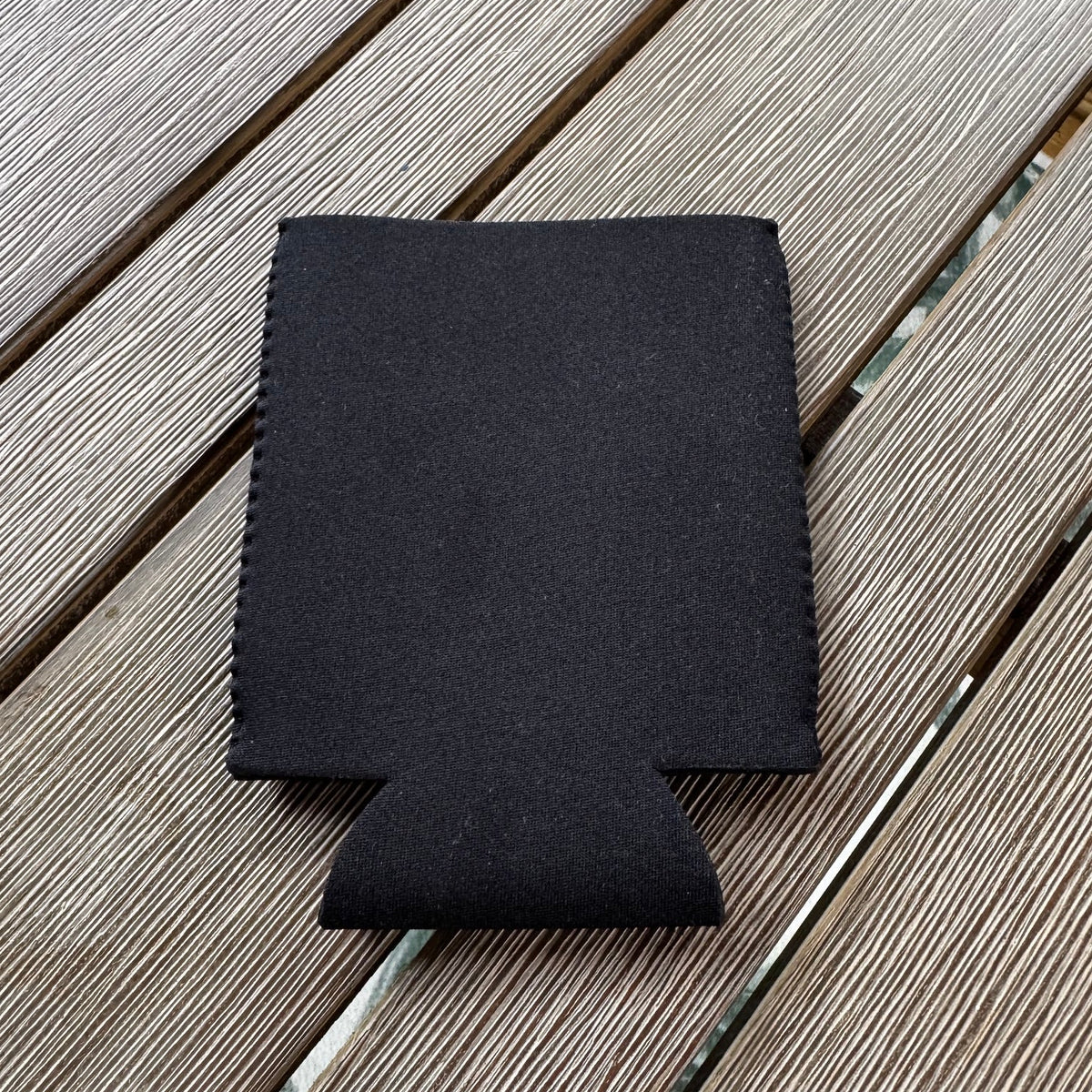Black FLOWAV koozie can cooler showing the back on a weathered outdoor table