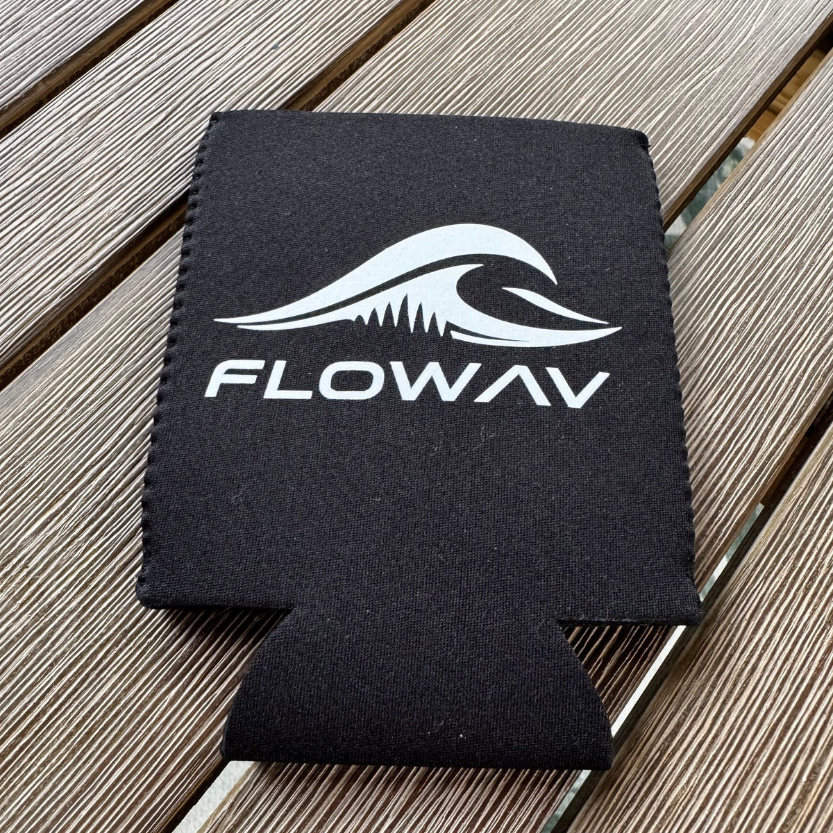 Black FLOWAV neoprene can cooler with white wave logo on an outdoor wood table.