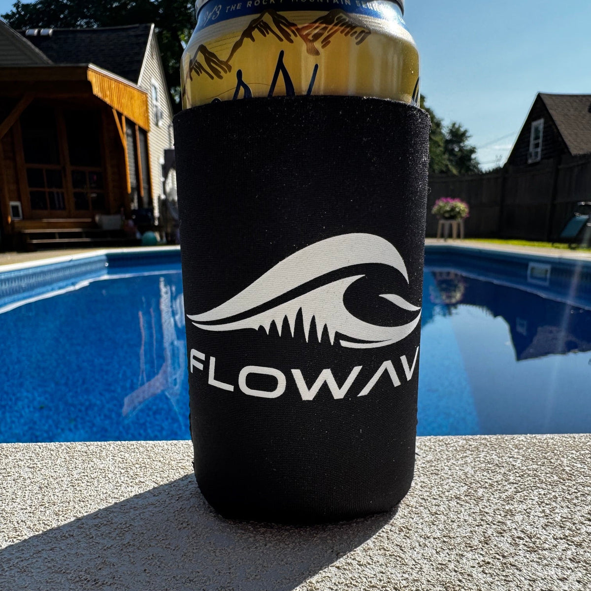 Black FLOWAV neoprene can cooler with white wave logo holding a beverage can outdoors by a pool.