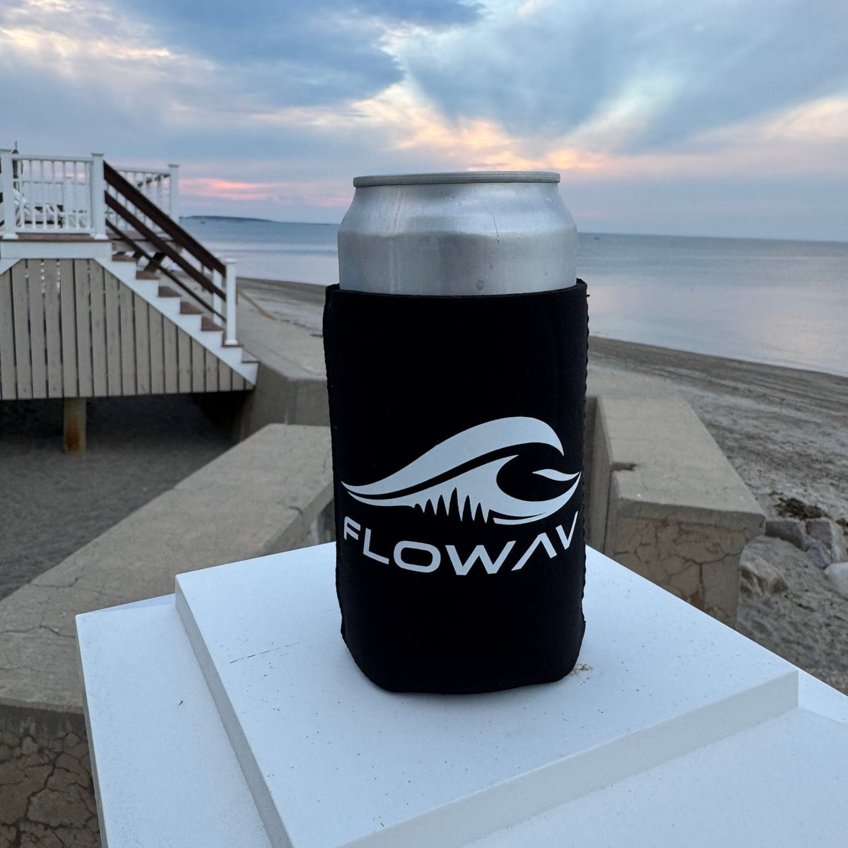 Black FLOWAV can cooler holding a silver can near the beach at sunset.