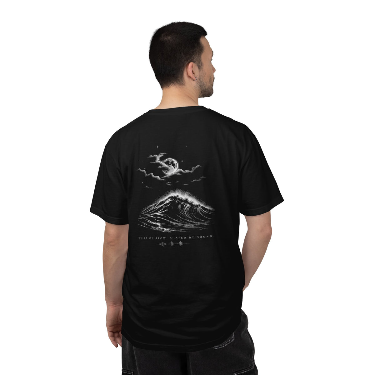 Man wearing a FLOWAV Midnight Edition Graphic Tee in Black showing the back graphic featuring a moonlit ocean wave breaking with a full moon, clouds and stars in the sky.