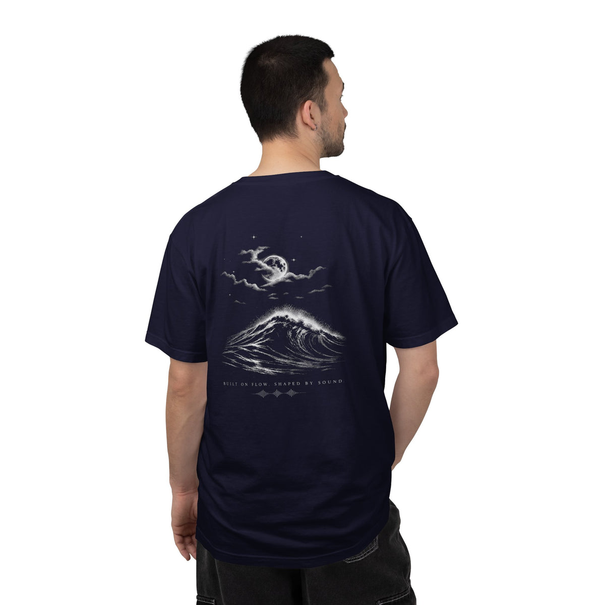 Man wearing the FLOWAV Midnight Edition Graphic Tee in True Navy showing the back graphic of a moonlit wave break with Built on Flow. Shaped by Sound. underneath it. The sky is a full moon and clouds with stars.