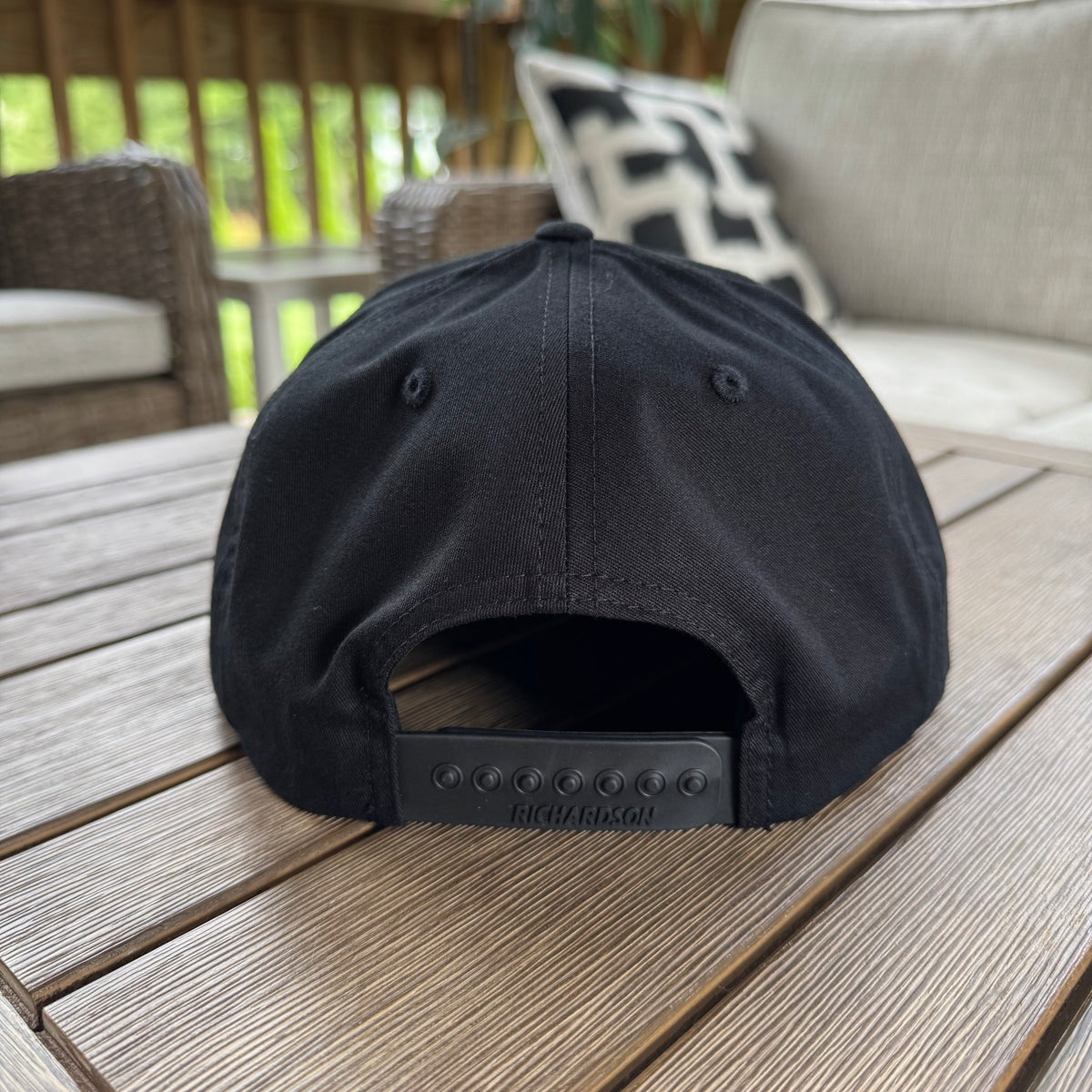 A FLOWAV Midnight Edition Richardson R255 showing the back snapback adstable hat feature in black. Set on a weathered wood outdoor table