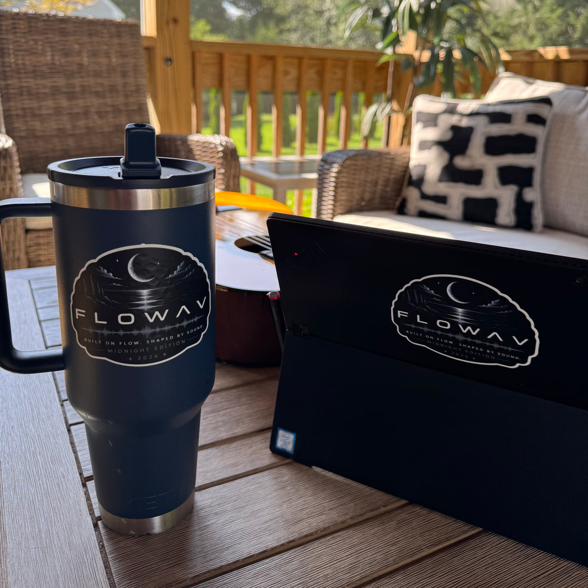 FLOWAV Midnight Edition Vinyl Stickers on a dark blue tumbler and the back of a laptop featuring a nighttime scene of a moon over the water. There is a guitar in the background and nature scenery.