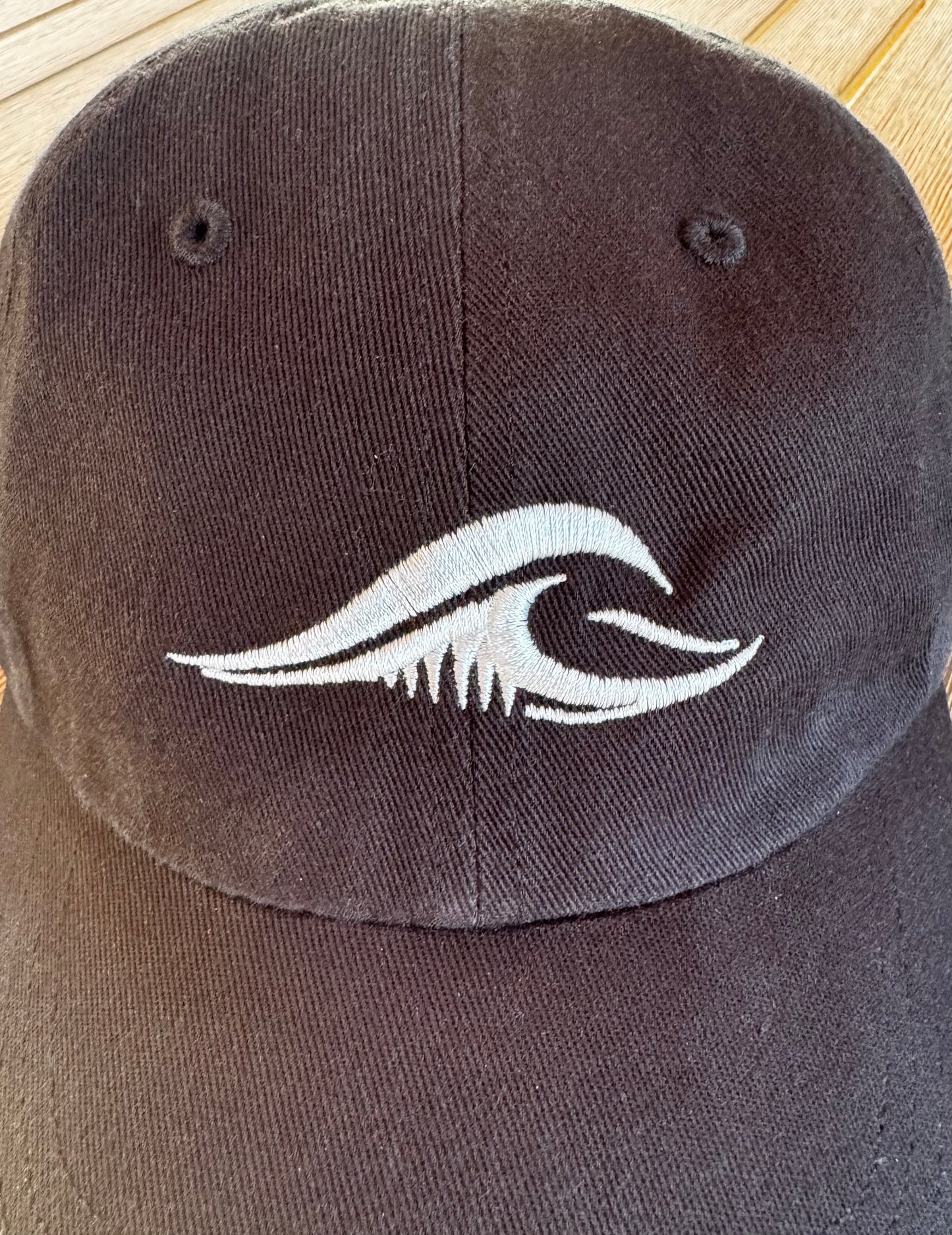 Close-up of the FLOWAV wave logo embroidered in cream thread on a black Richardson R55 baseball hat