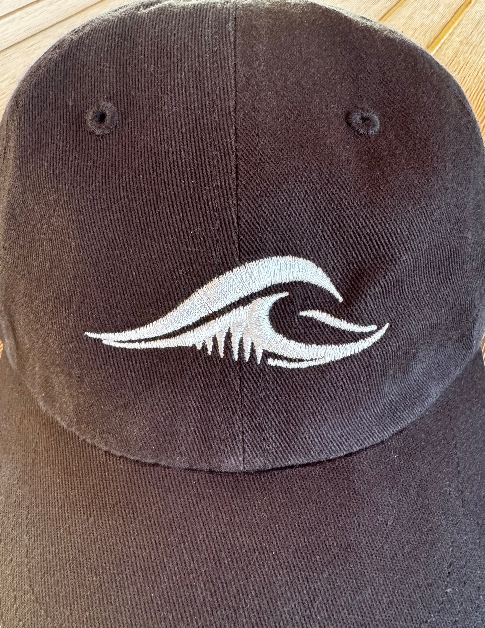 Close-up of the FLOWAV wave logo embroidered in cream thread on a black Richardson R55 baseball hat