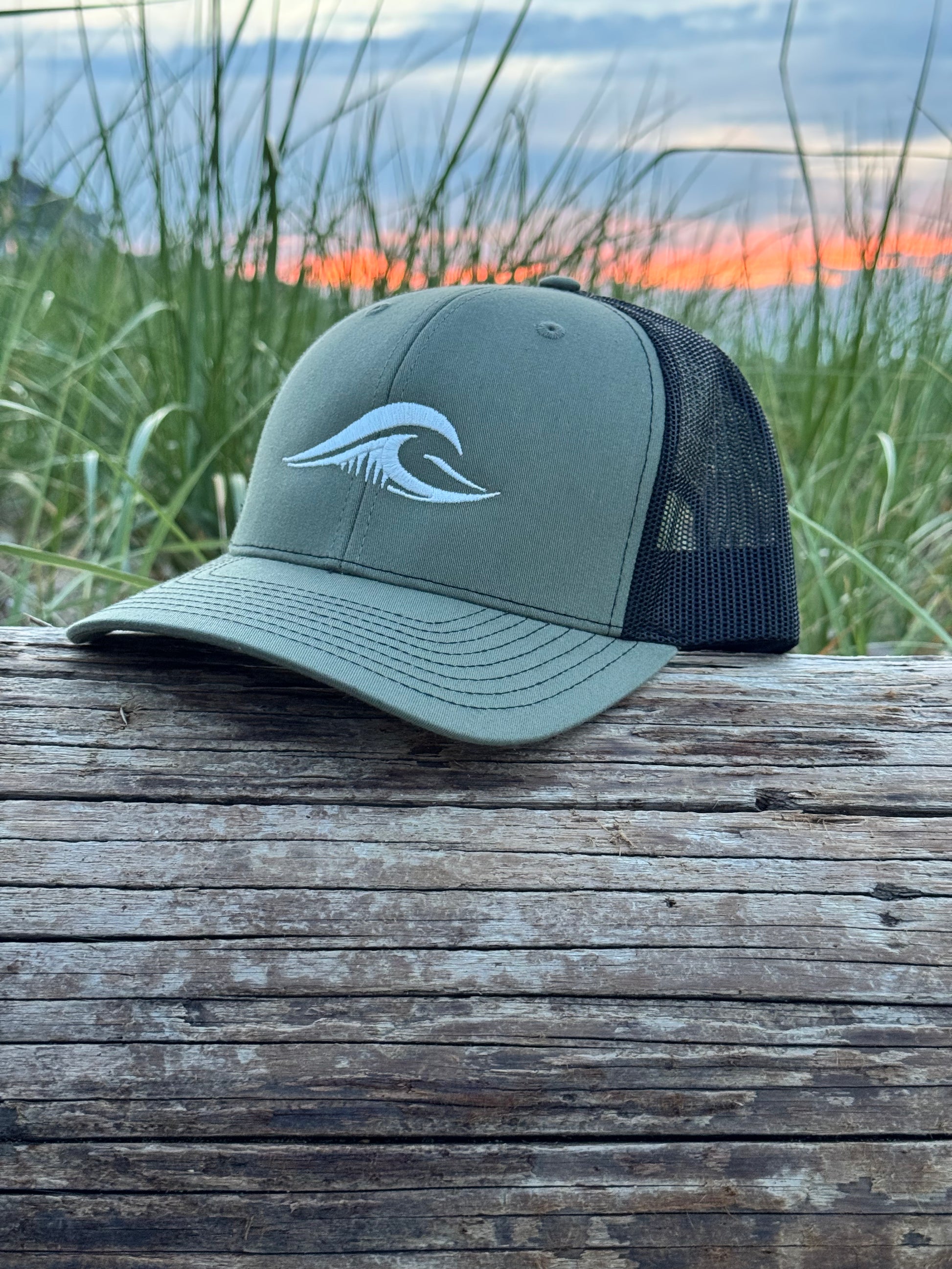 Loden Black FLOWAV Richardson 112 Trucker Hat with cream wave logo on weathered driftwood overlooking the beach at sunset