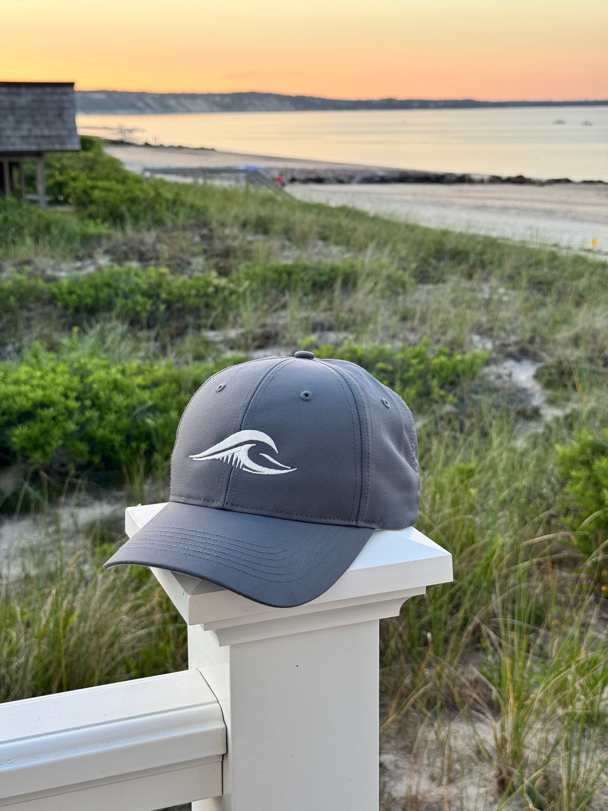 FLOWAV Richardson R225 Performance Hat on a white fence overlooking the beach at sunset.