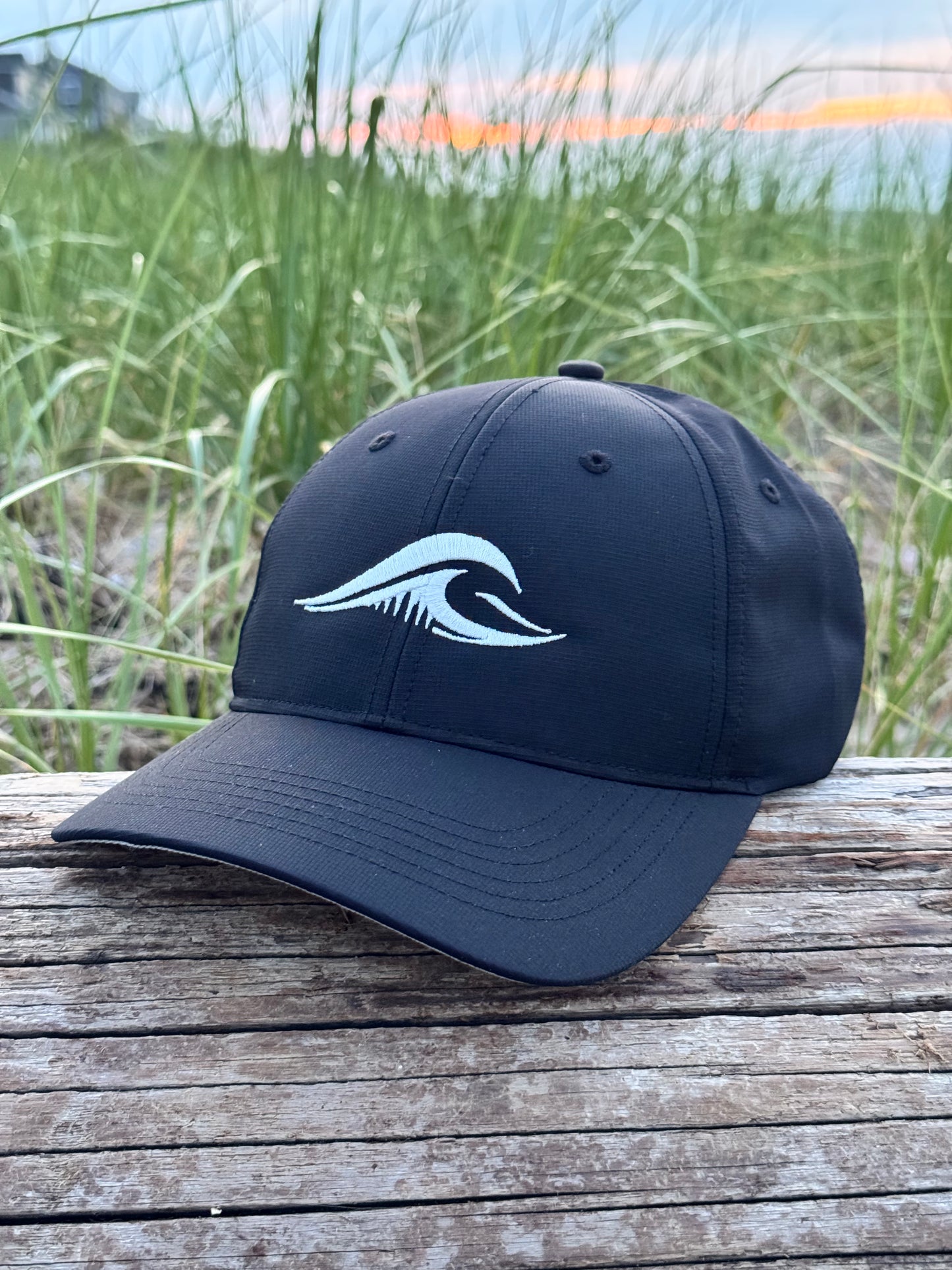 FLOWAV Richardson R225 Performance Hat resting on weathered driftwood with beach grass at sunset.