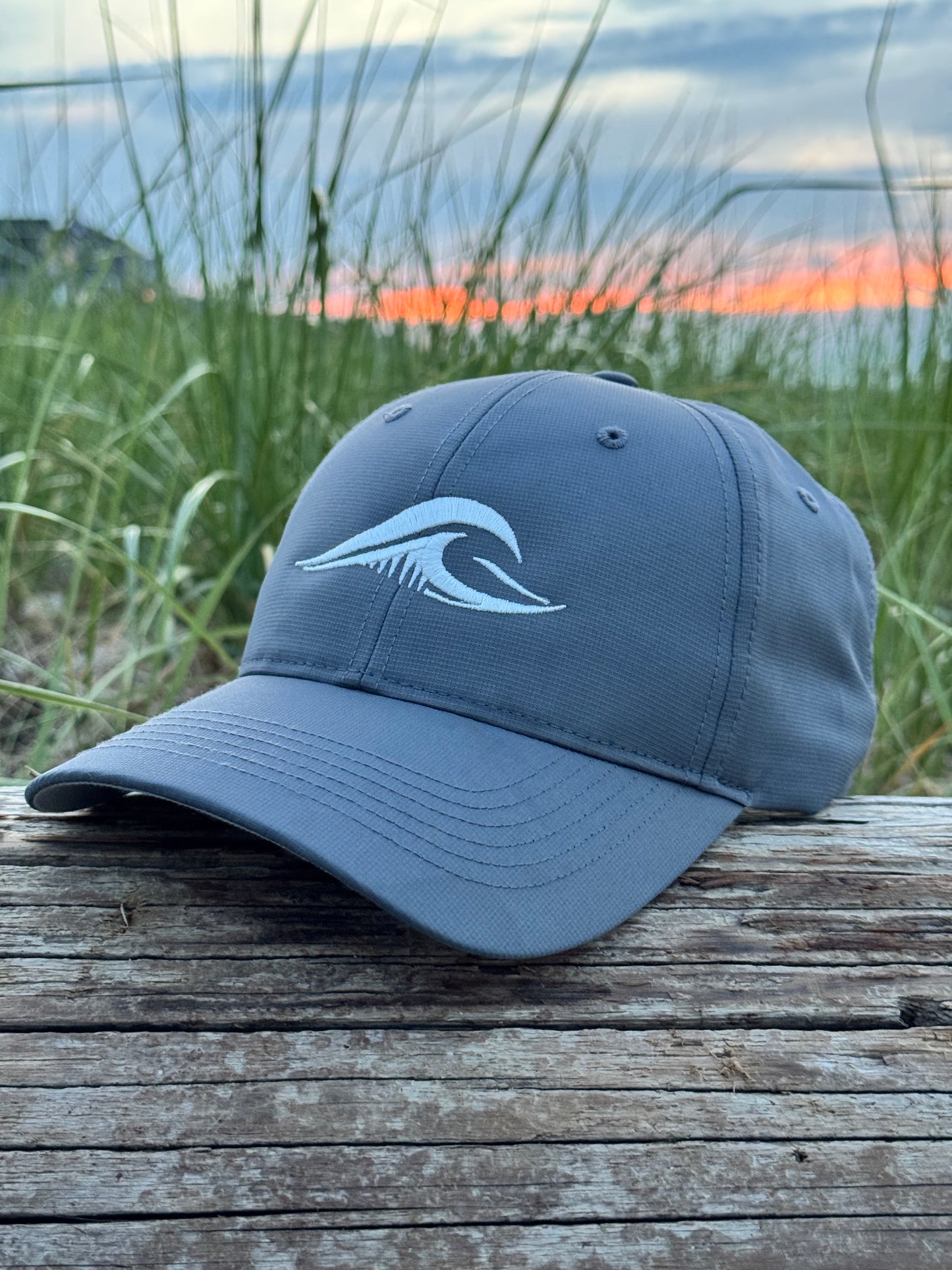 FLOWAV Richardson R225 Performance Hat resting on weathered driftwood with beach grass at sunset.