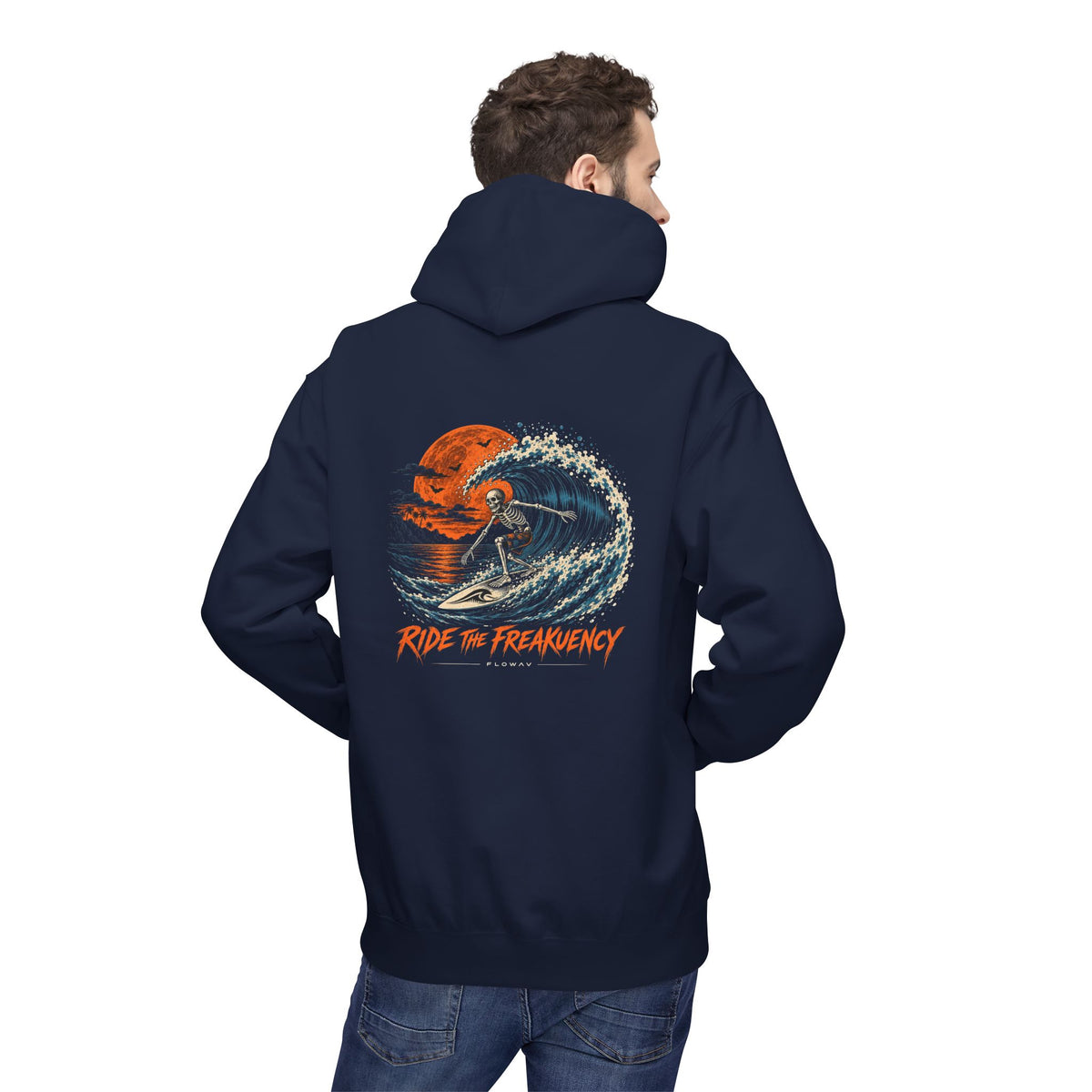 A man wearing the FLOWAV Ride the Freakuency Hoodie in navy showing a skeleton surfing a wave and an orange moon.